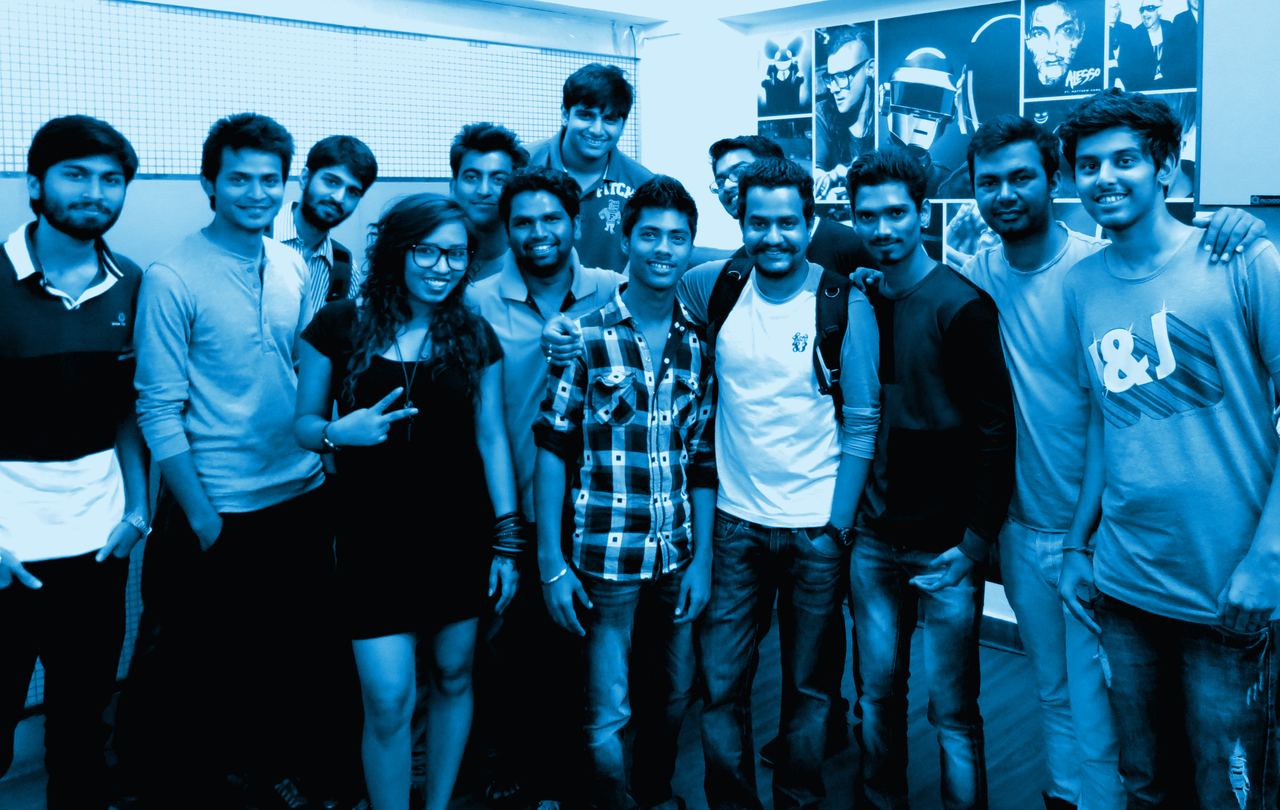 A group of Audioqube students smiling together in front of a wall of DJ posters