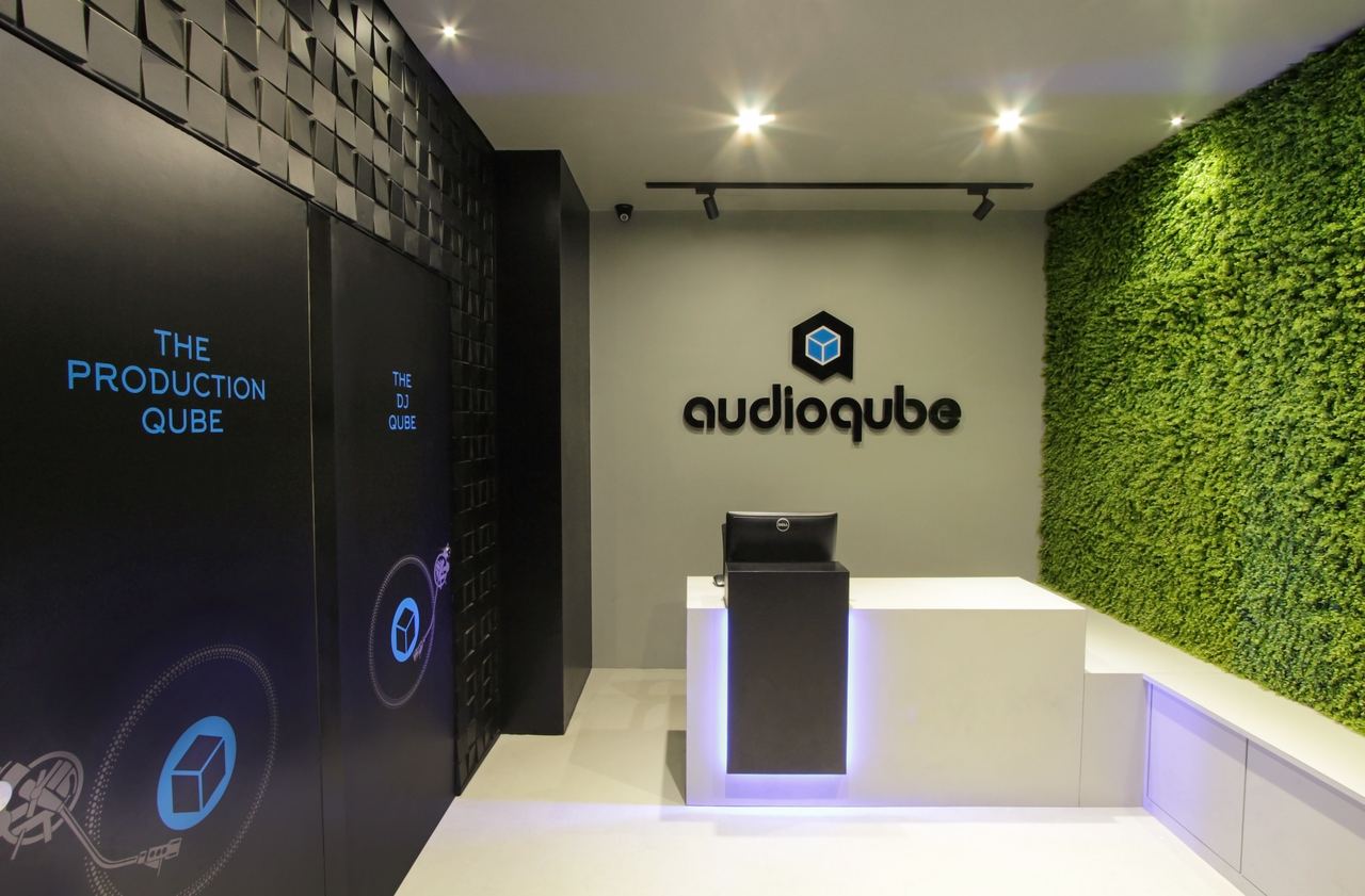 Audioqube main reception: the backlit Audioqube logo on a black wall, a white desk and a green living wall