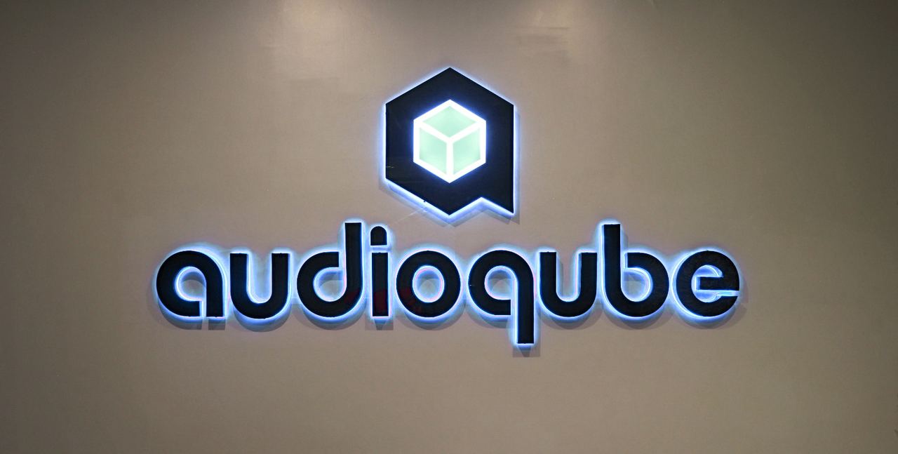 The Audioqube logo sign, backlit in blue, on a grey wall at the academy